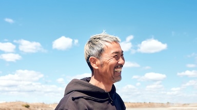 Man smiling set in front of a blue sky with clouds